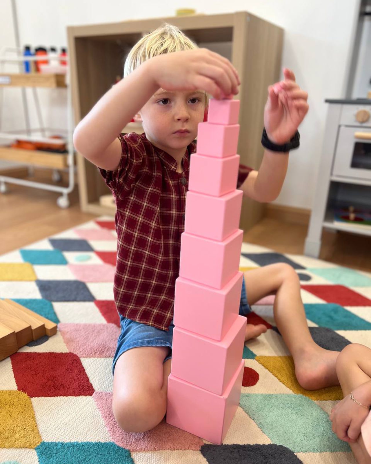 A child building the Montessori pink tower at Little & Loved