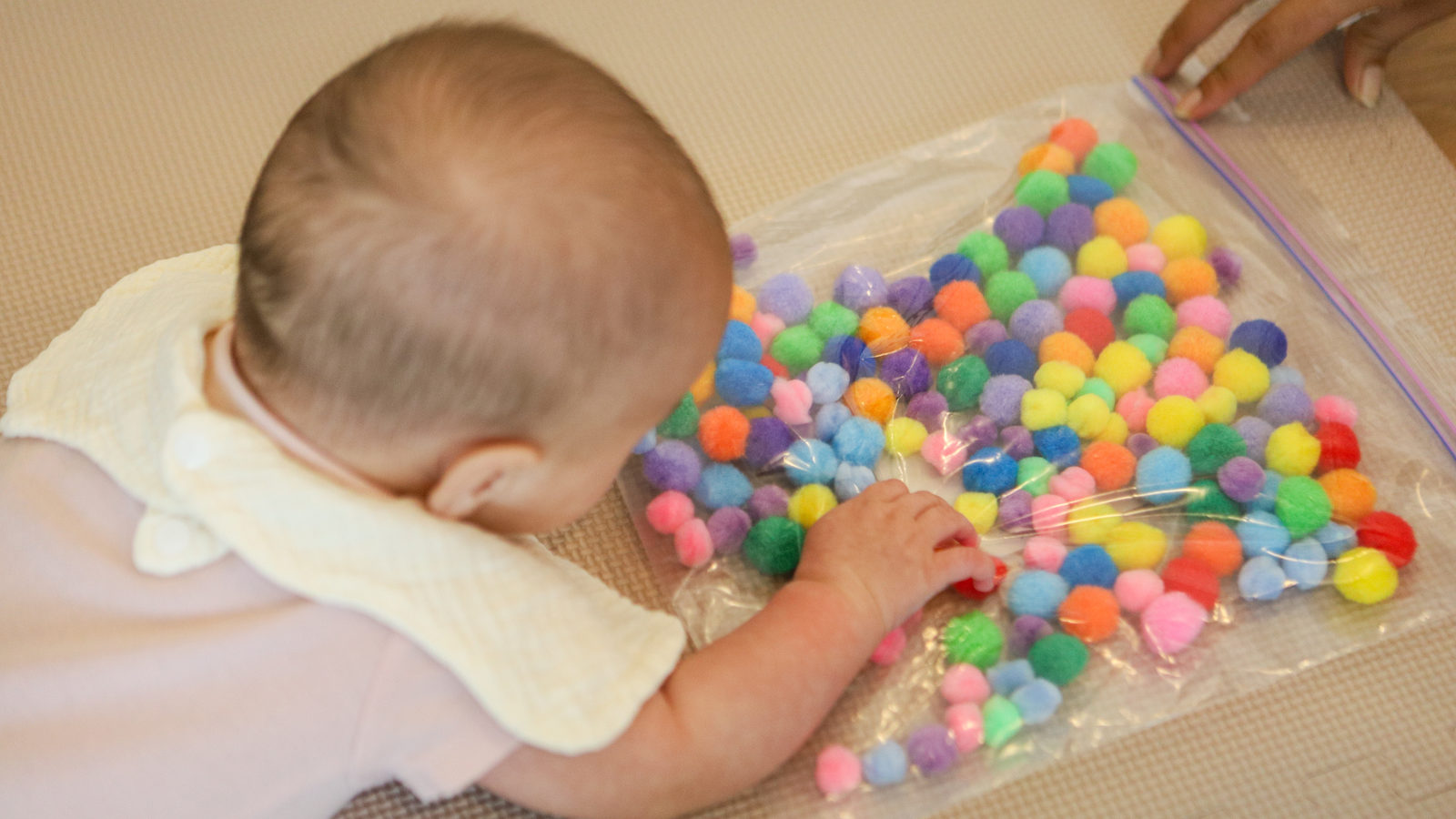 An infant exploring a colourful sensory bag at Little & Loved