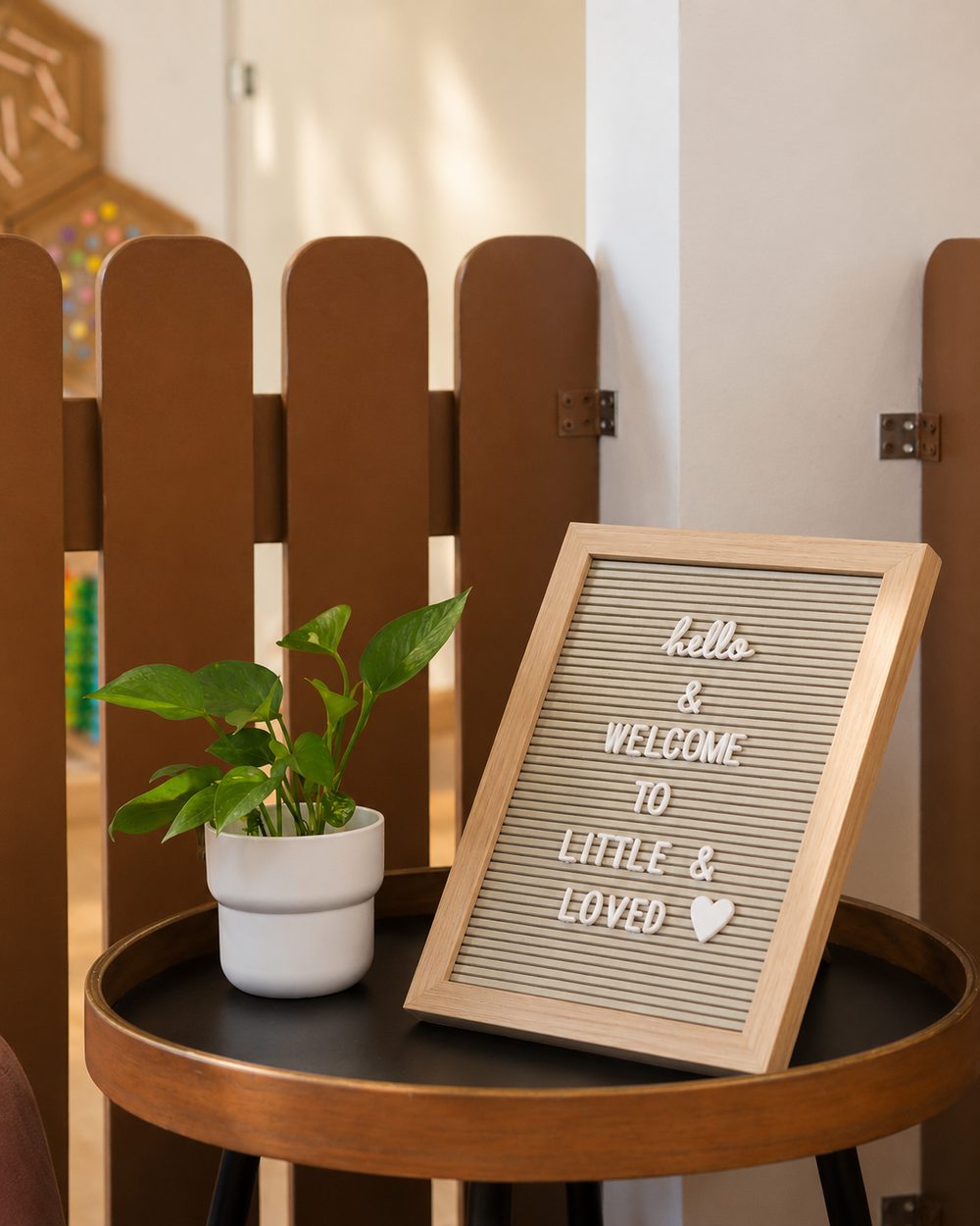 A “hello & welcome to Little & Loved” letterboard sign beside a plant at the centre